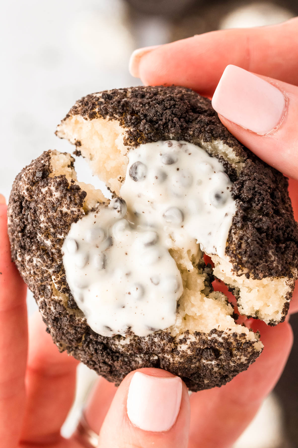 A woman's hand breaking an oreo thumbprint cookie in half.