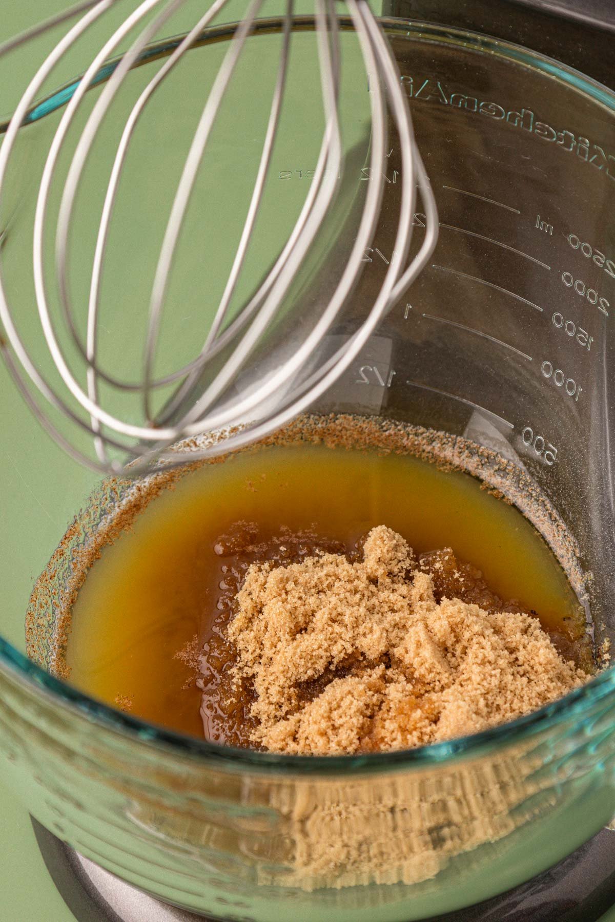 Brown sugar being added to browned butter in a glass mixing bowl.