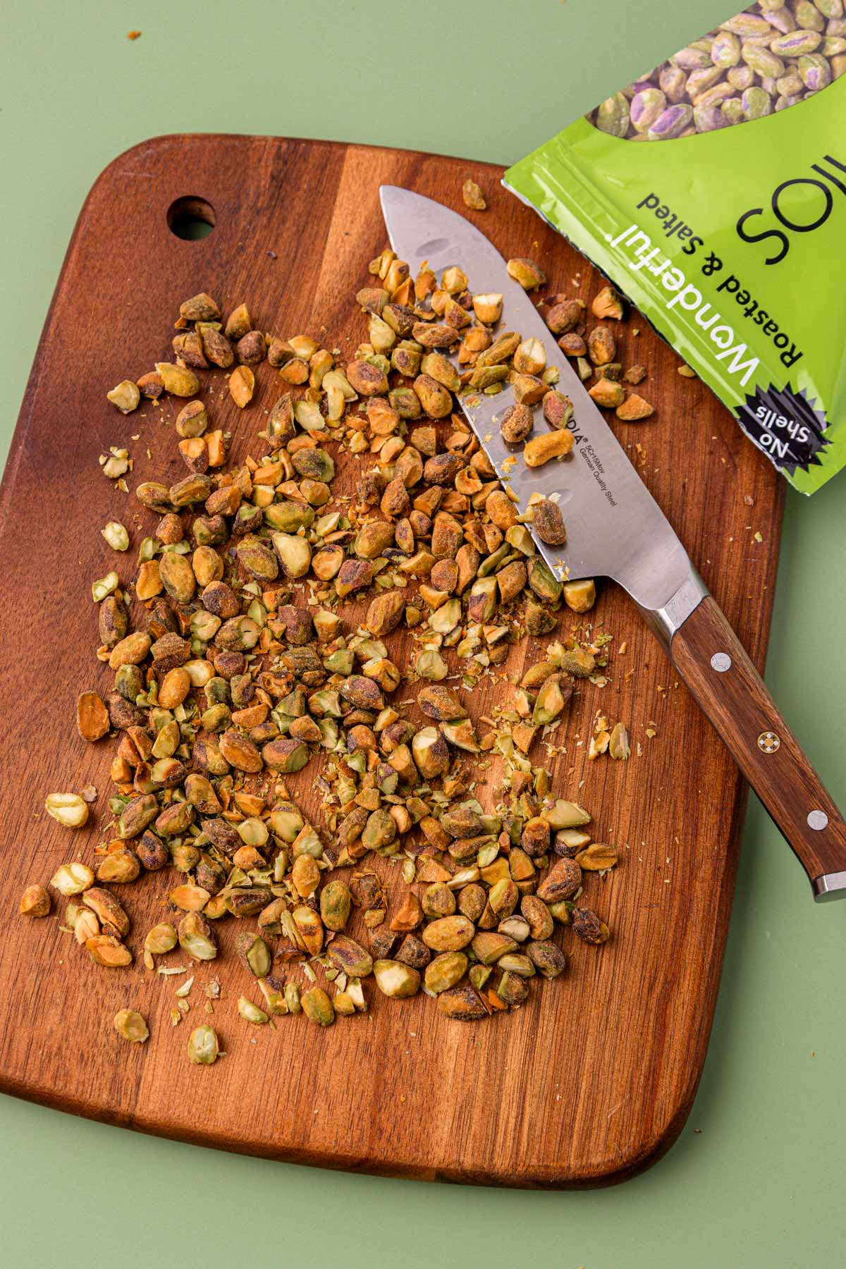 Pistachios being chopped on a wooden cutting board.