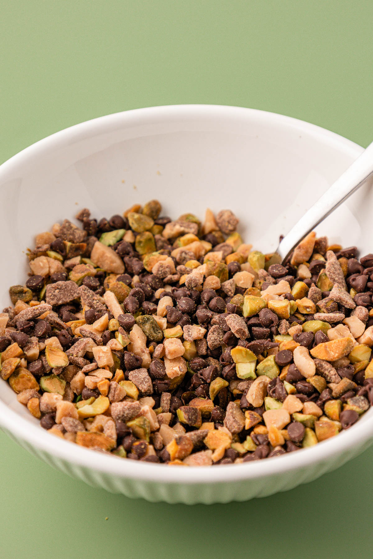 Chocolate chips, pistachios, and toffee mixed together in a white bowl.