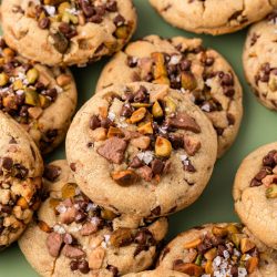 Close up of toffee chocolate chip and pistachio cookies scattered on a green surface.