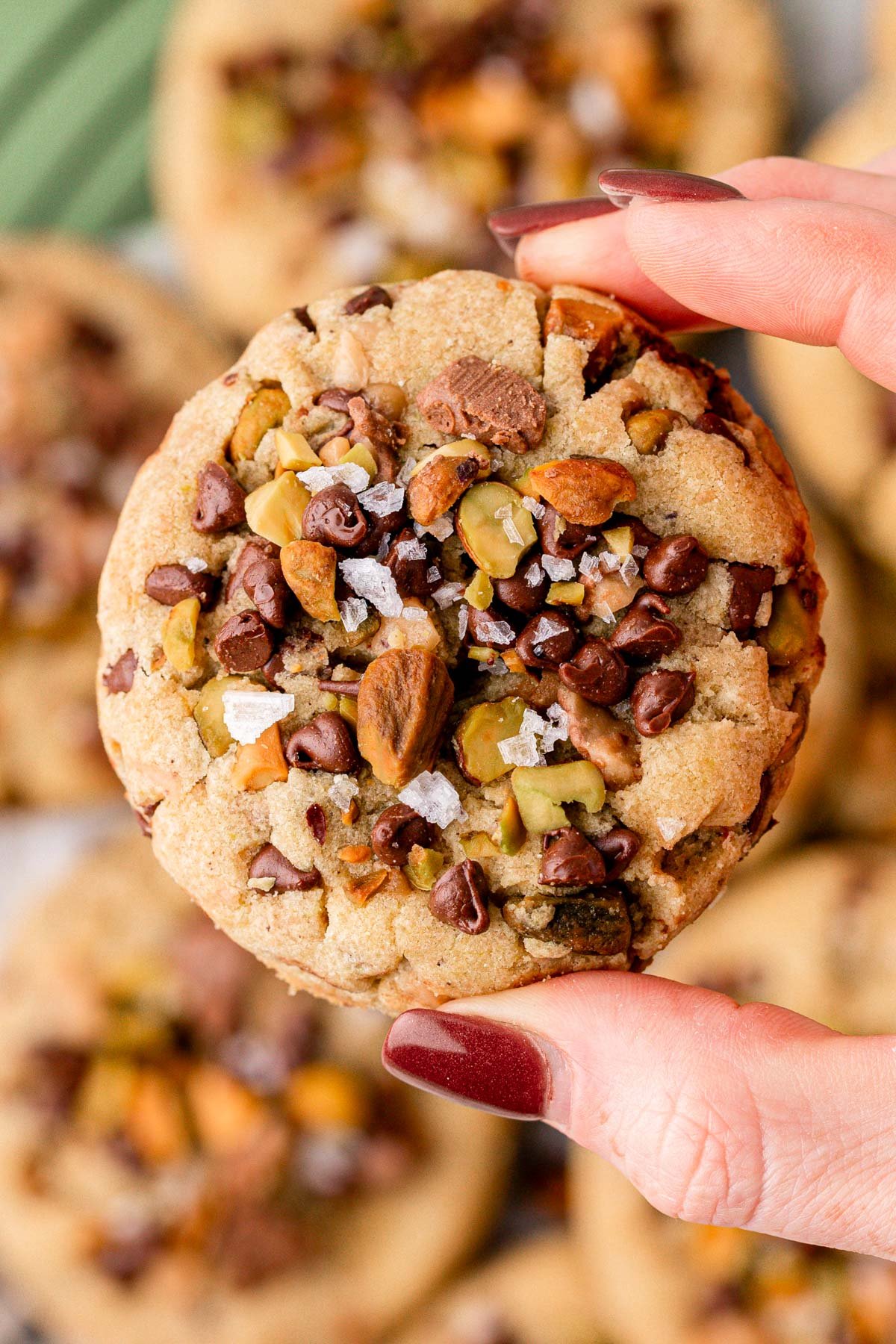 A woman's hand holding a toffee pistachio chocolate chip cookie.