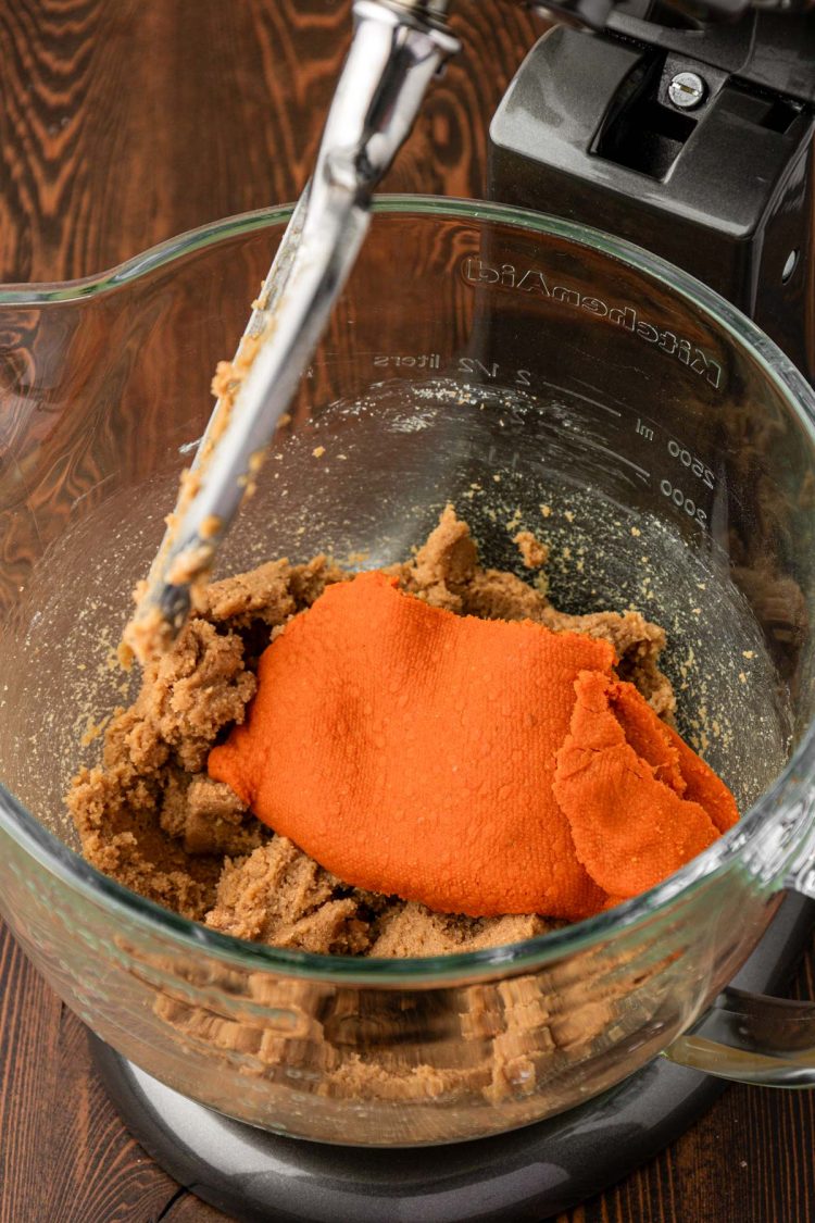 Pumpkin puree being added to cookie dough in a stand mixer.