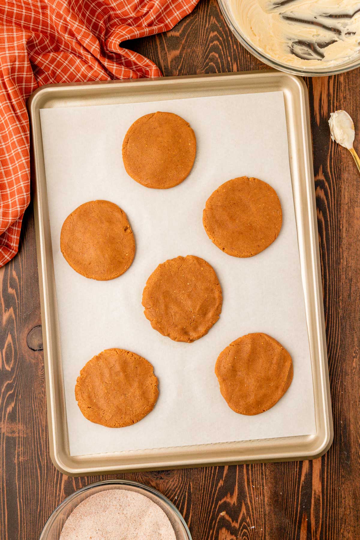 Pumpkin cookie dough circles on a parchment lined baking pan.