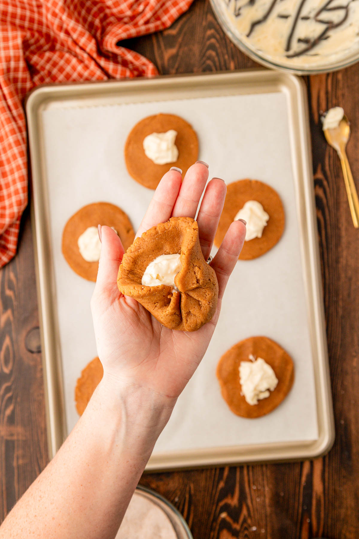 A woman's hand holding a pumpkin cookie dough wrapping around cream cheese filling.