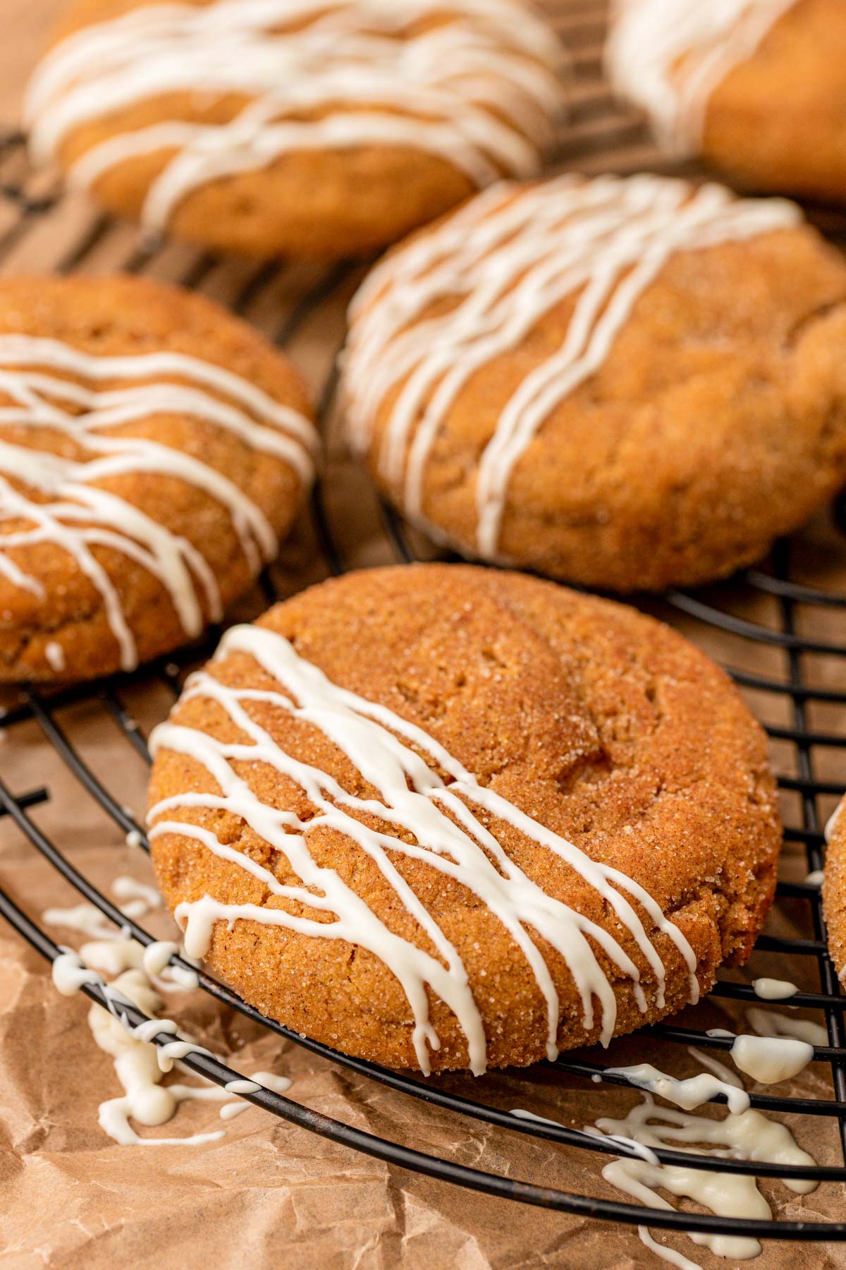 Pumpkin cookies with cheesecake filling and white chocolate drizzle on a wire rack.