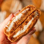 A woman's hand holding a pumpkin cheesecake cookie that's been split in half.