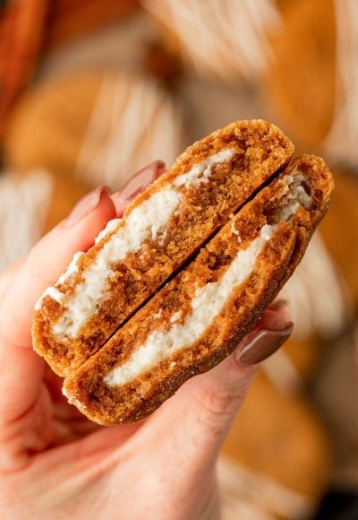 A woman's hand holding a pumpkin cheesecake cookie that's been split in half.