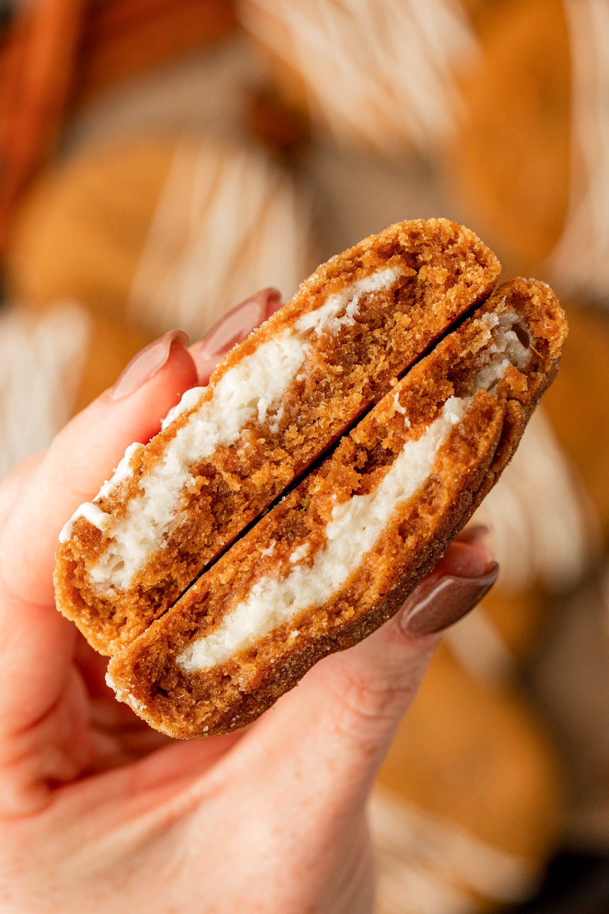 A woman's hand holding a pumpkin cheesecake cookie that's been split in half.