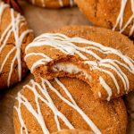 Pumpkin cheesecake cookies drizzled in white chocolate on parchment paper. One missing a bite.