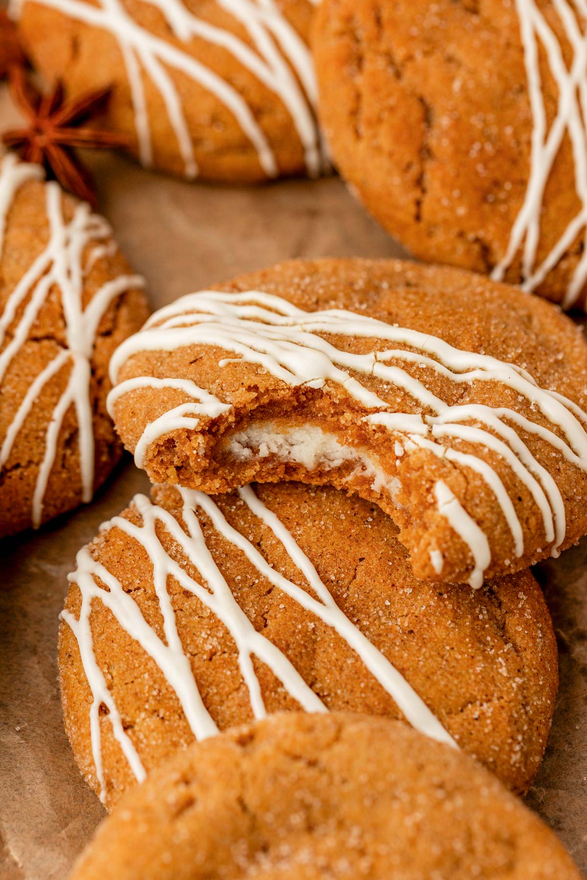 Pumpkin cheesecake cookies drizzled in white chocolate on parchment paper. One missing a bite.