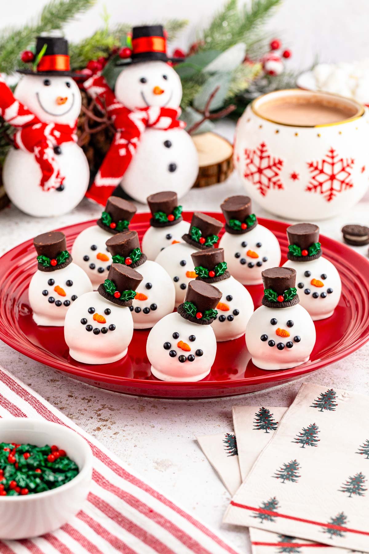 Red plate on a table with holiday decor filled with Snowman oreo truffles.