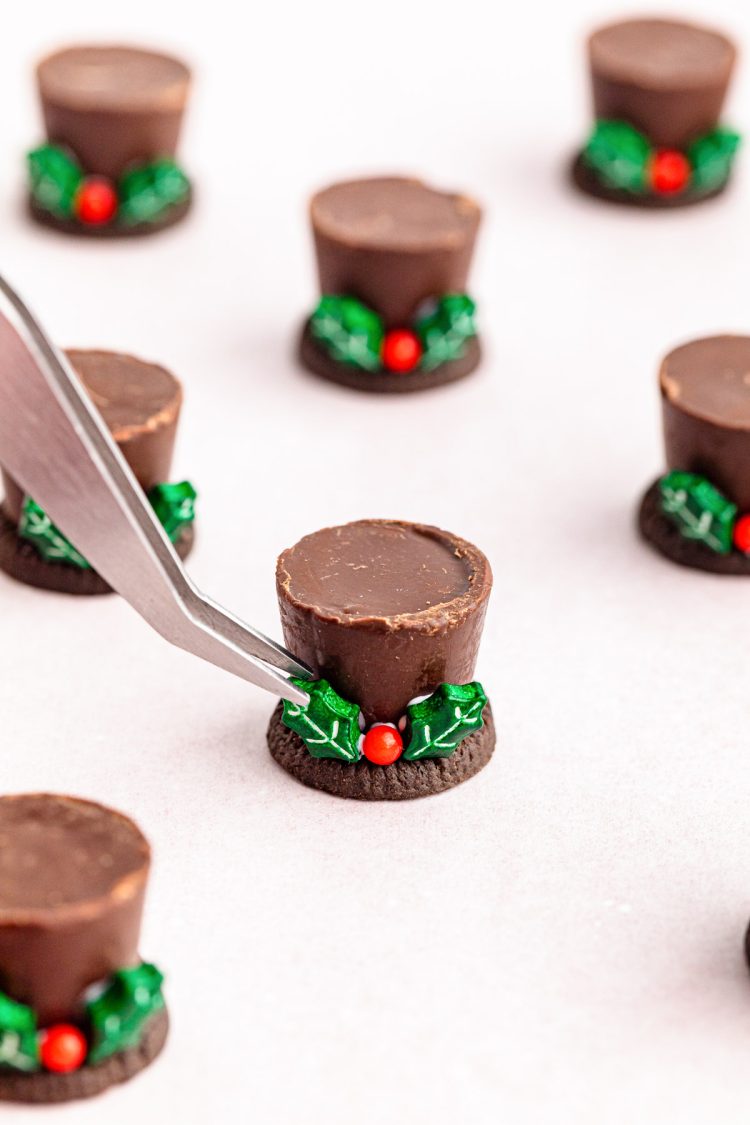 Food tongs placing sprinkles on a chocolate hat.