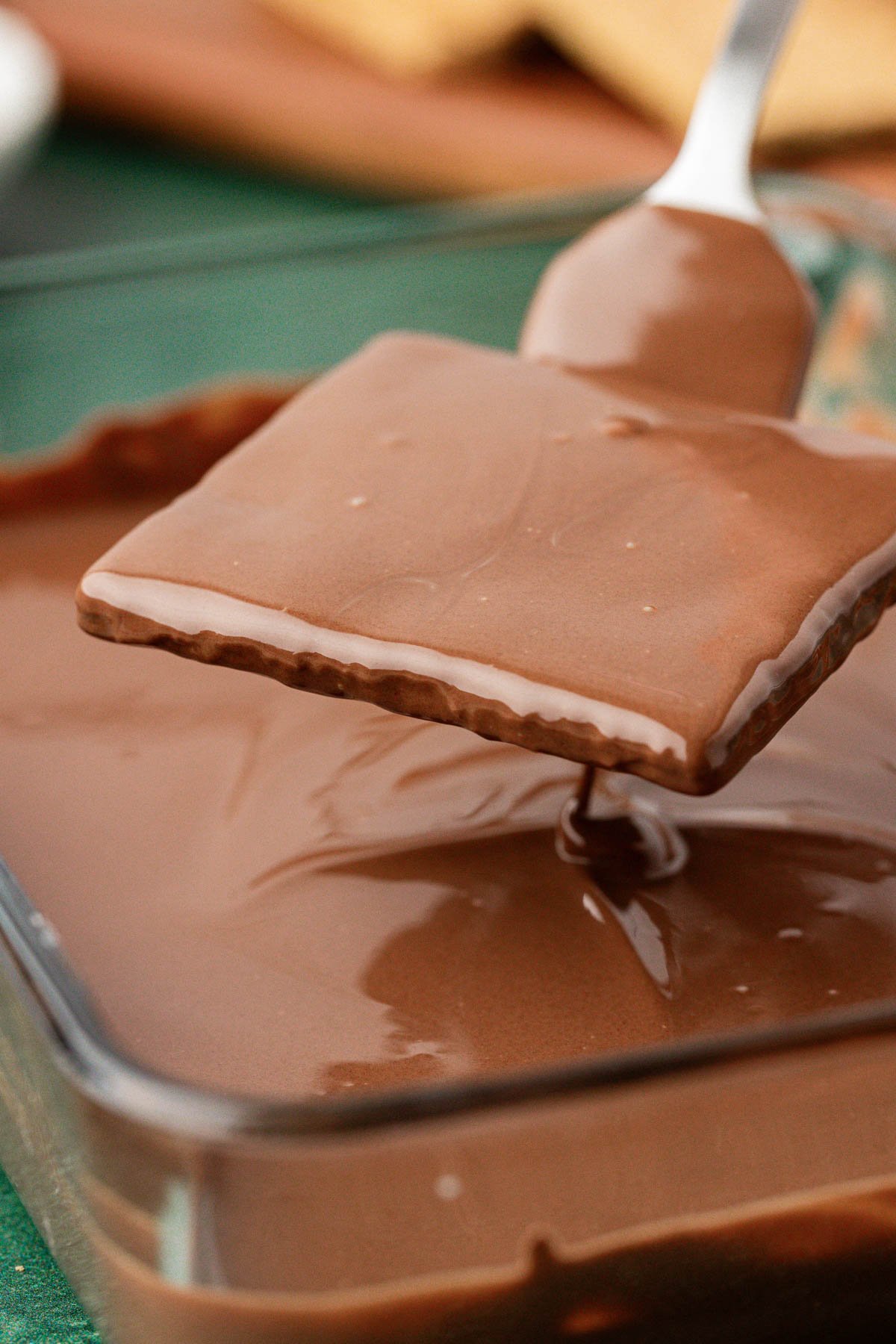 A graham cracker being lifted out of a dish of melted chocolate.