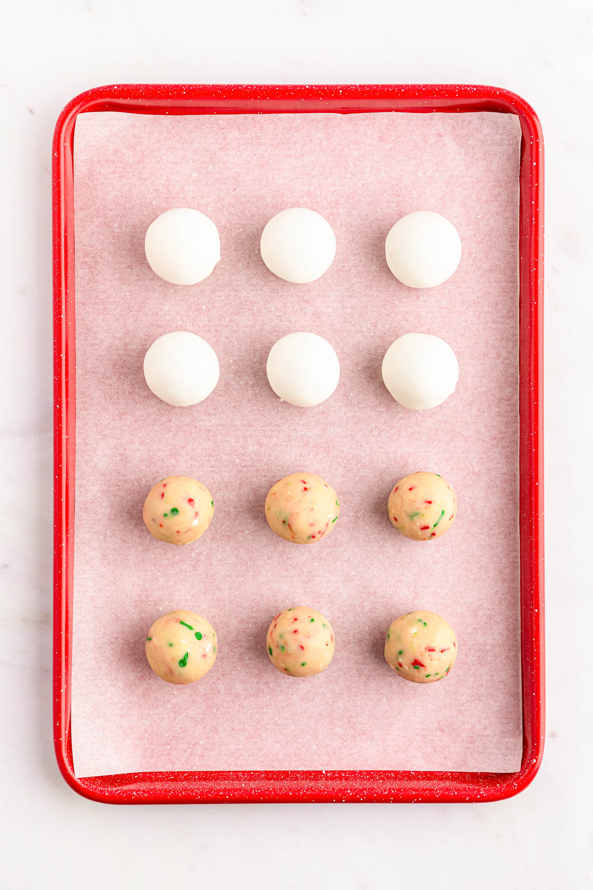 Sugar cookie balls on a parchment lined baking sheet, some dipped in white chocolate.