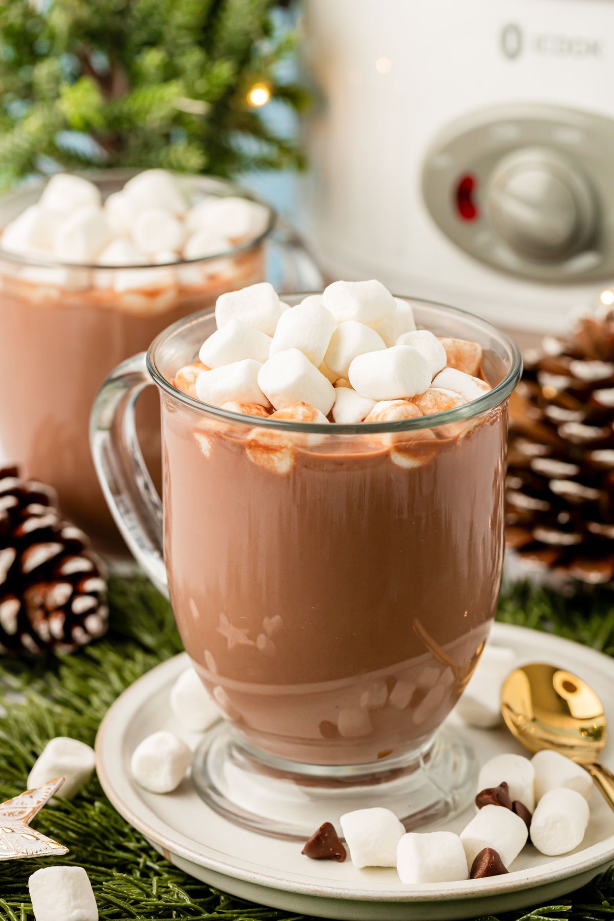 Two mugs in front of a crockpot filled with hot chocolate.