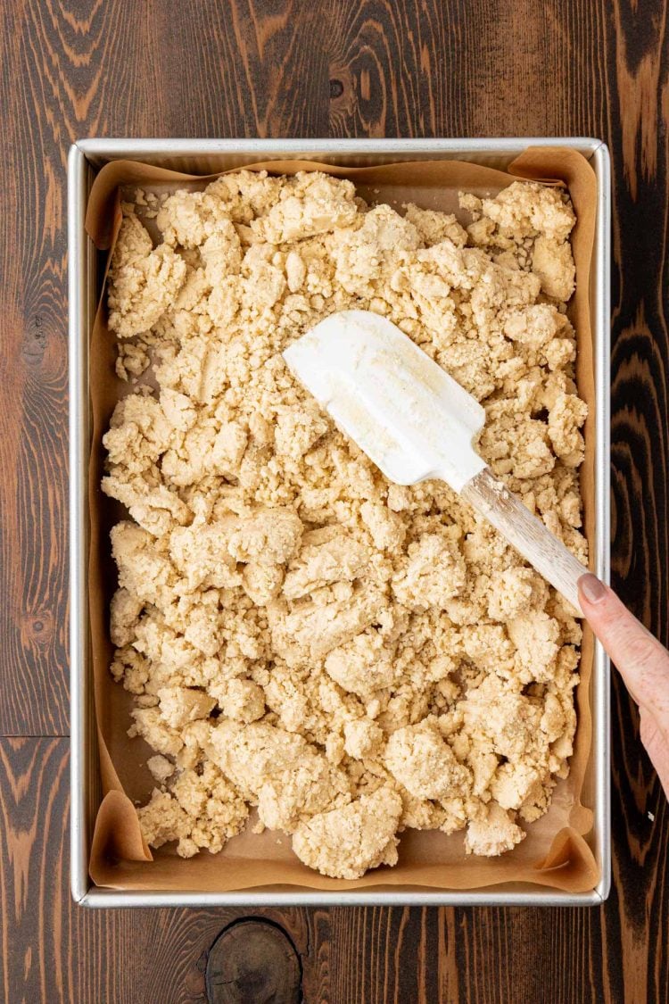 Shortbread cookie dough in a pan being pressed with a rubber spatula.