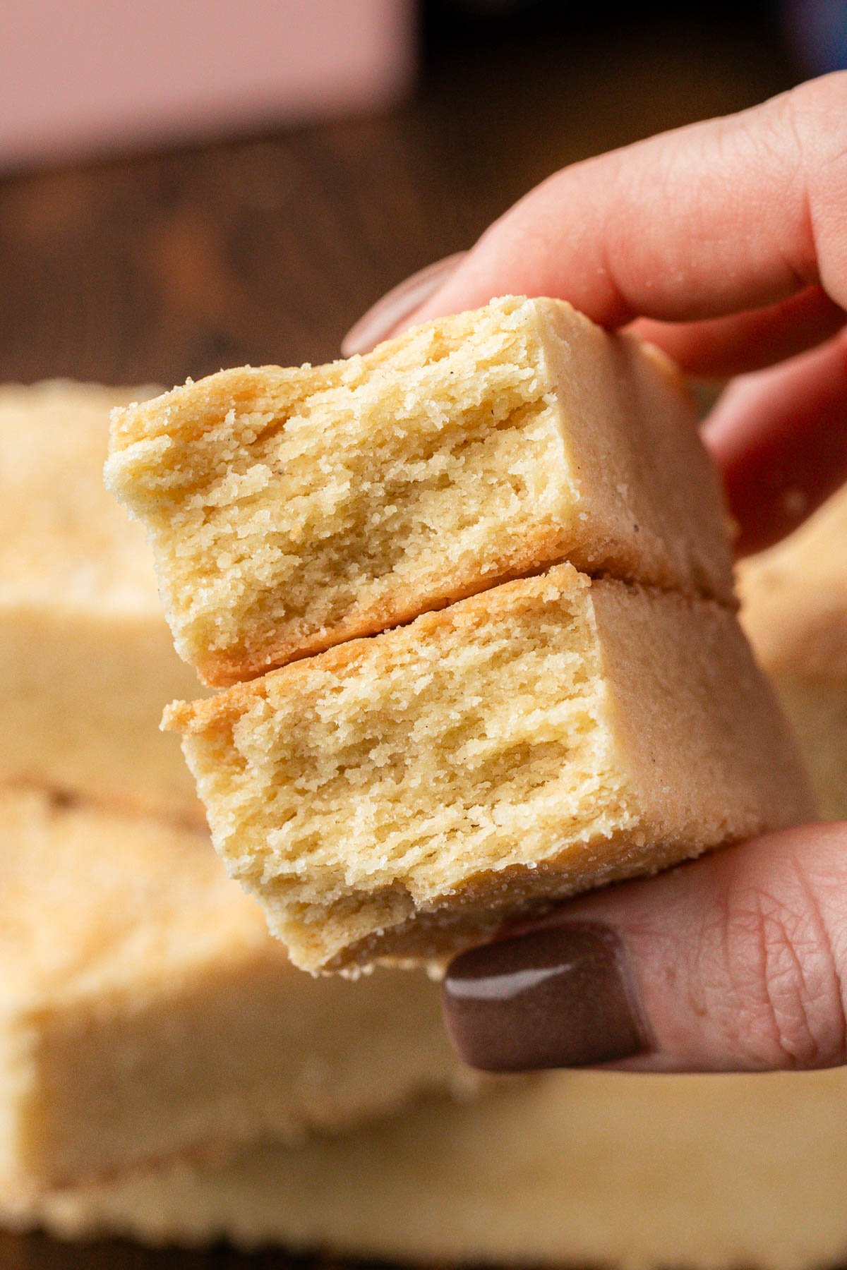 A woman's hand holding shortbread biscuits to the camera that have been broken in half to show texture.