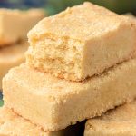 Close up of shortbread cookie bars stacked on a wooden table.
