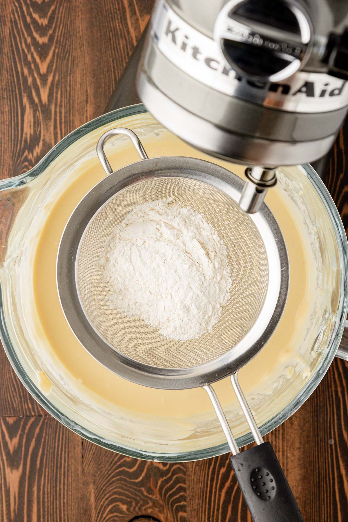 Flour being sifted into cheesecake filling mixture in a mixing bowl.