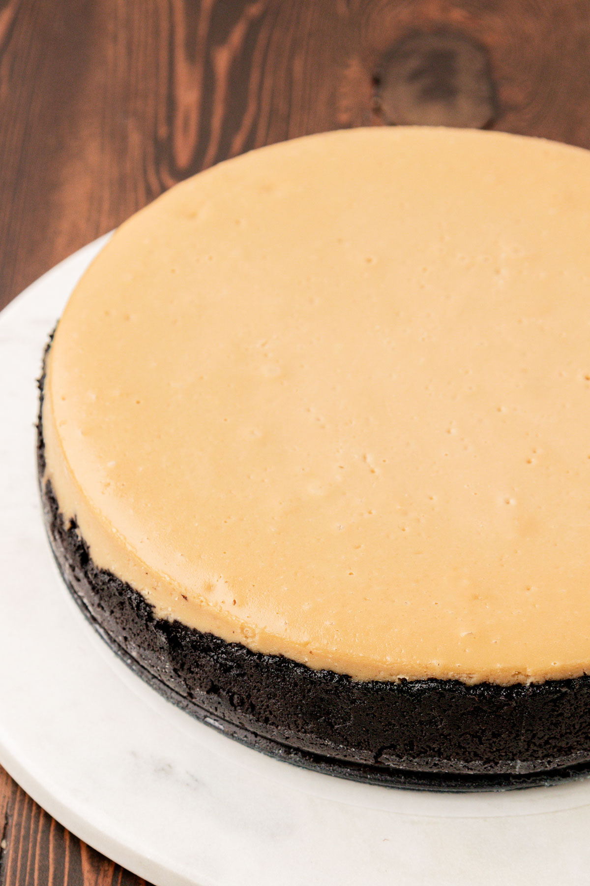 A coffee cheesecake on a white cake stand ready to be topped.