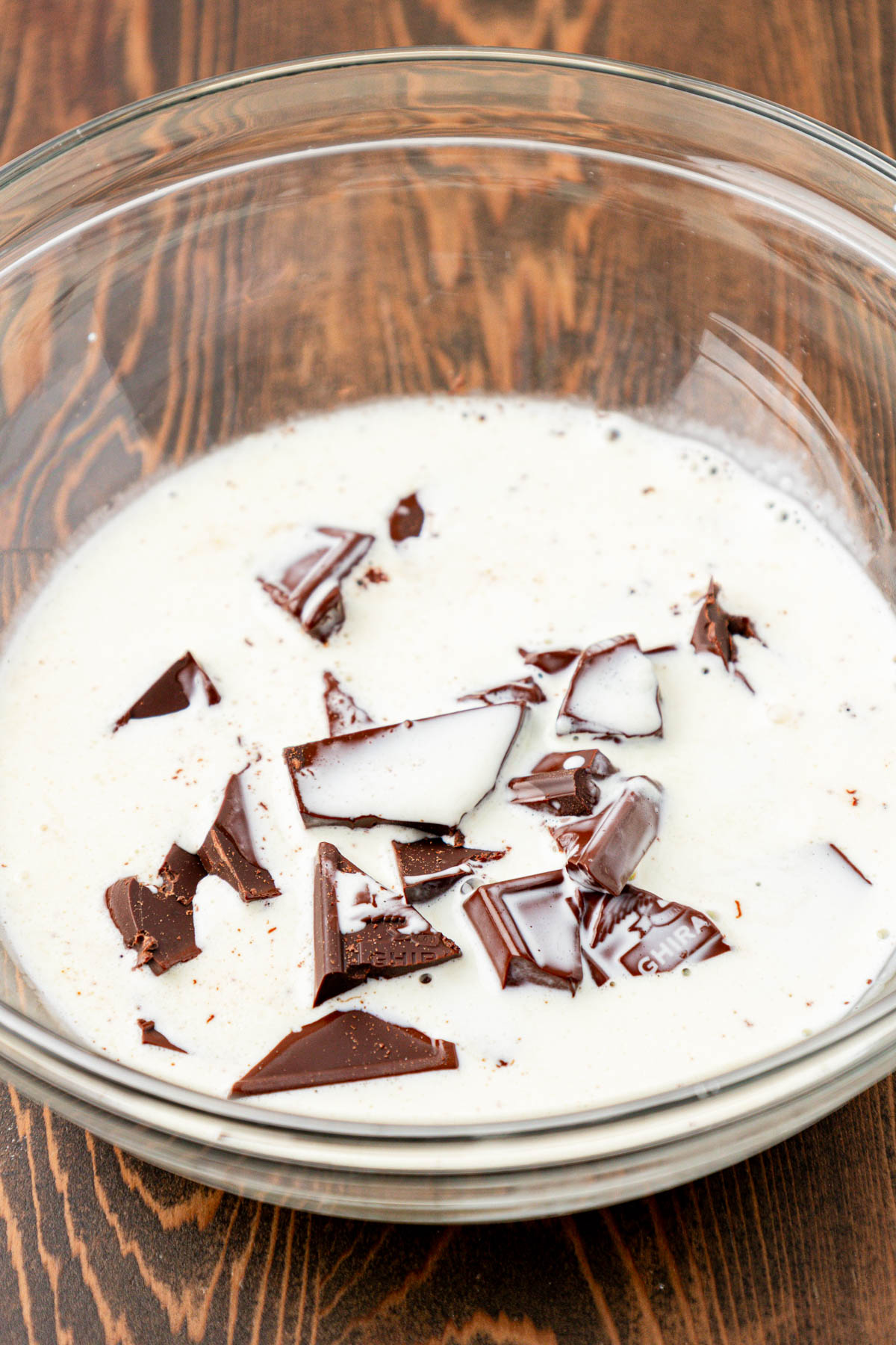 Chopped chocolate and heavy cream in a glass mixing bowl.
