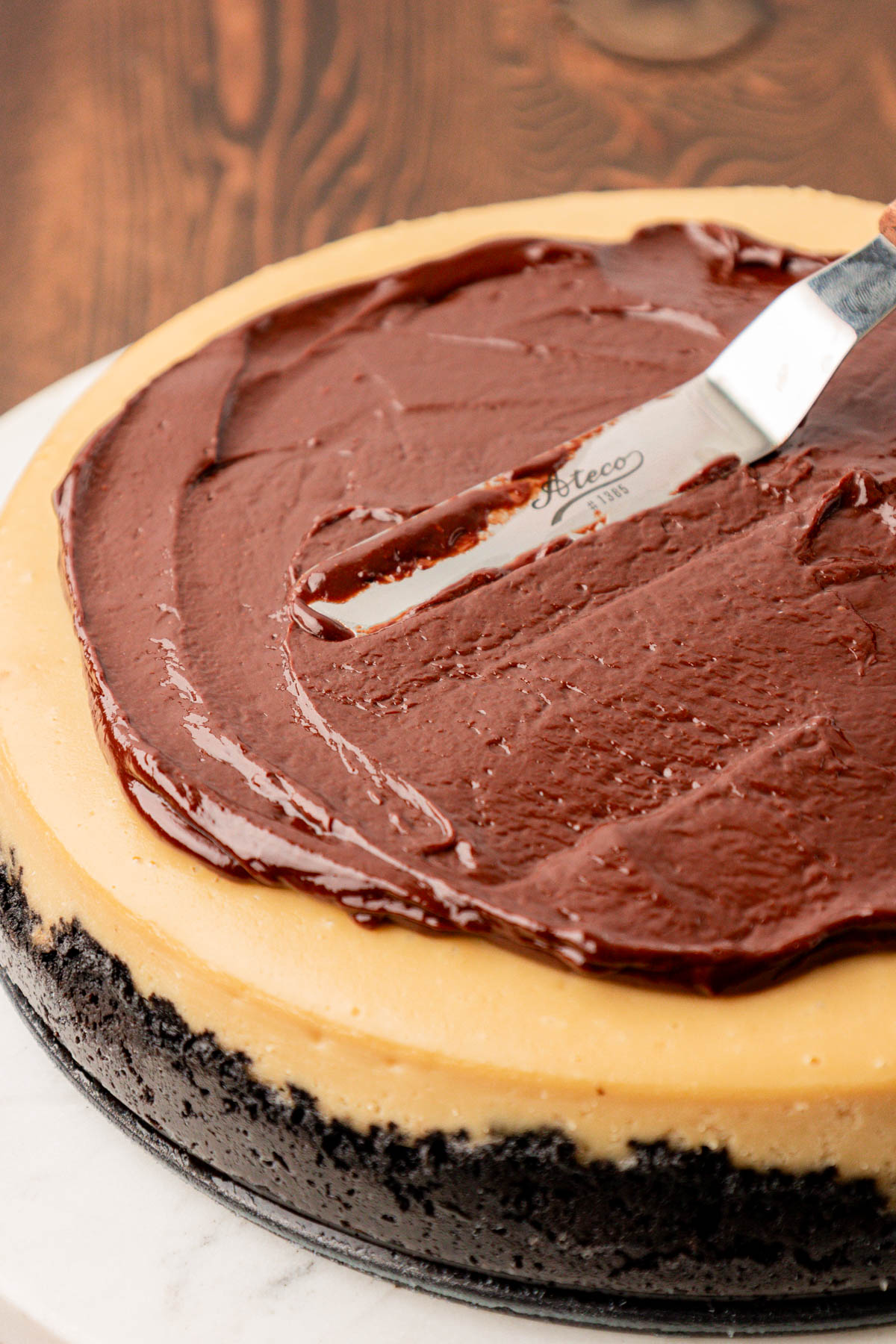 Chocolate ganache being spread over the top of a coffee cheesecake.