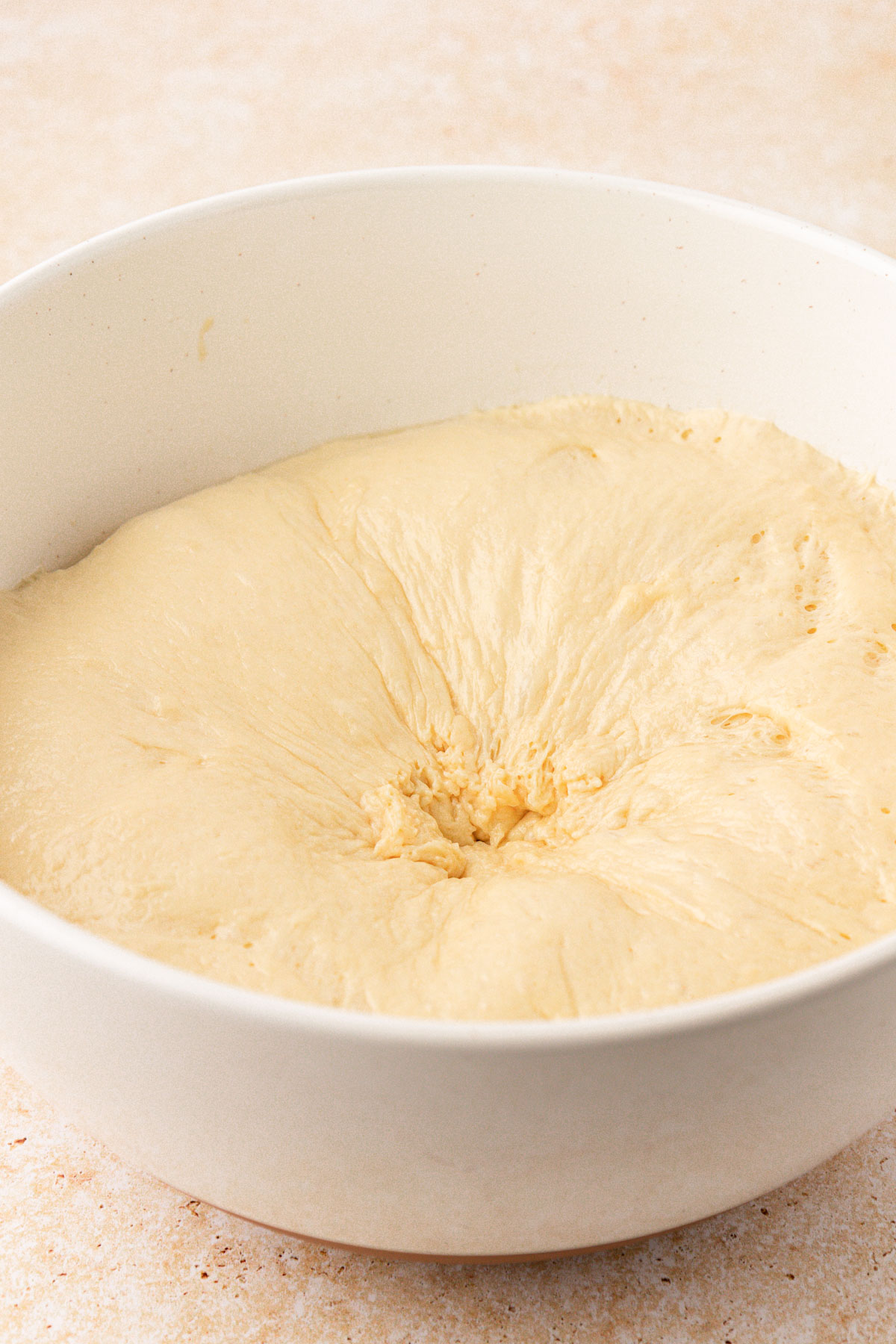 Cinnamon roll dough that has been punched down in a white bowl.