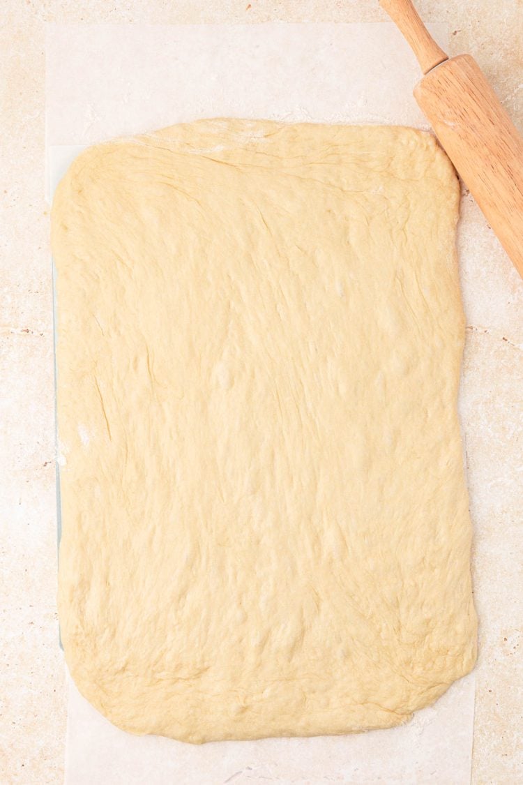 Dough being rolled out to make cinnamon rolls on a surface.