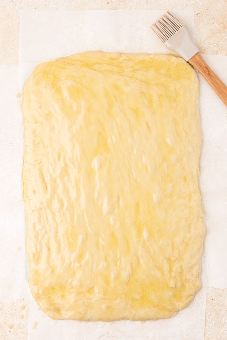 Cinnamon roll dough that's been brushed with butter and rolled out on a table.