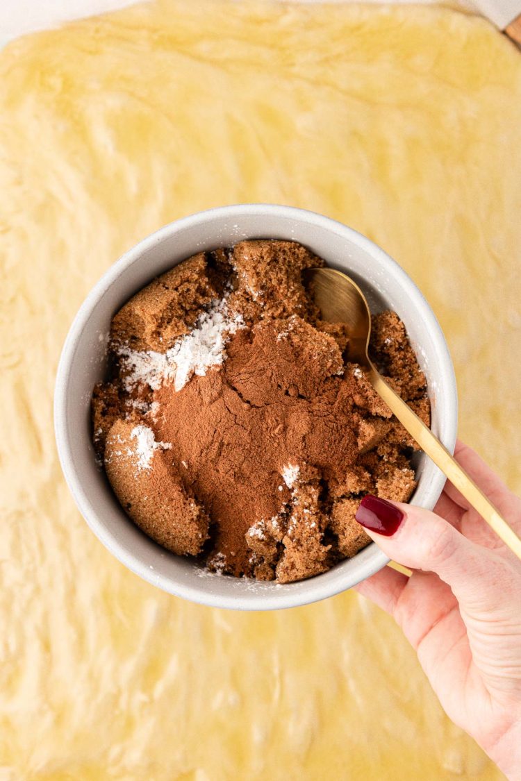 A woman's hand holding a small bowl of cinnamon rolls filling ingredients.