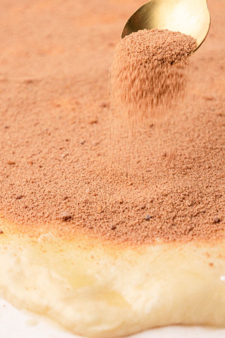 Cinnamon roll filling being sprinkled on cinnamon roll dough.