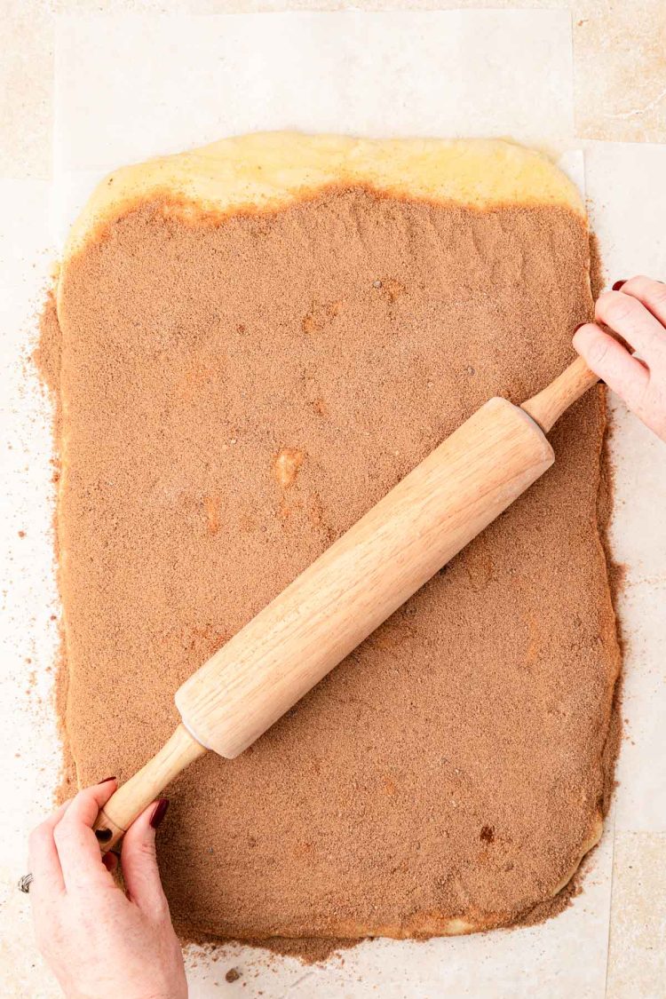 A rolling pin rolling cinnamon roll sugar filling into the dough.