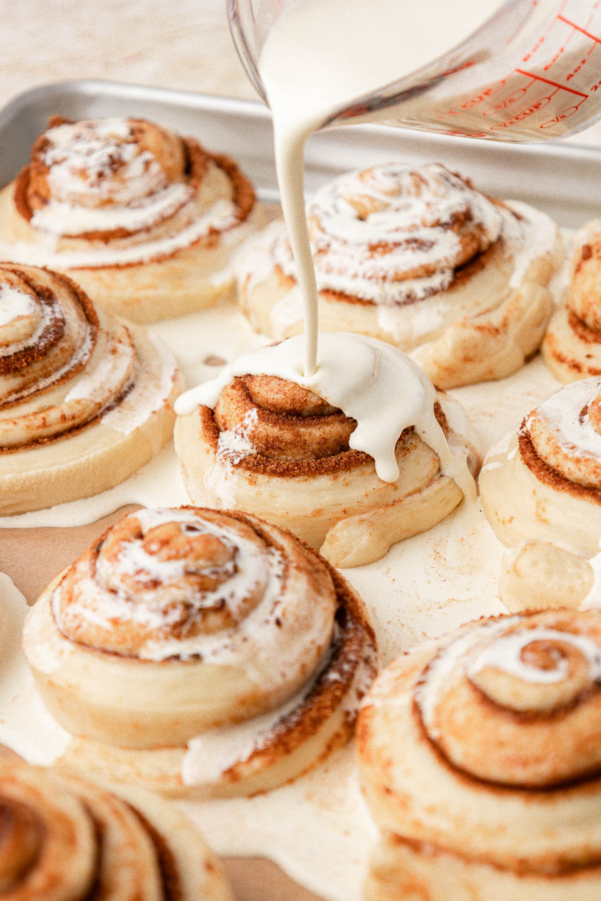 Heavy cream being poured over the top of the cinnamon roll.s