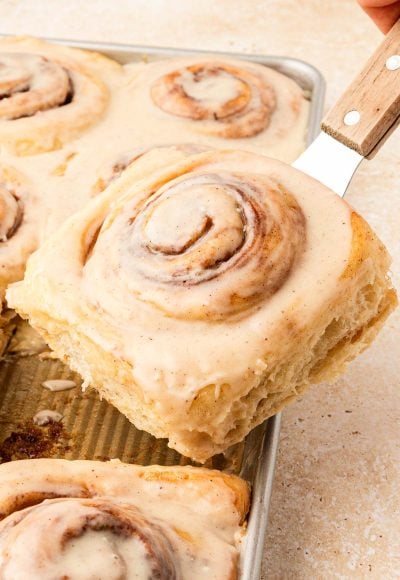 Cinnamon roll being lifted out of a pan with a spatula.