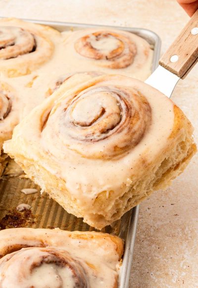 Cinnamon roll being lifted out of a pan with a spatula.