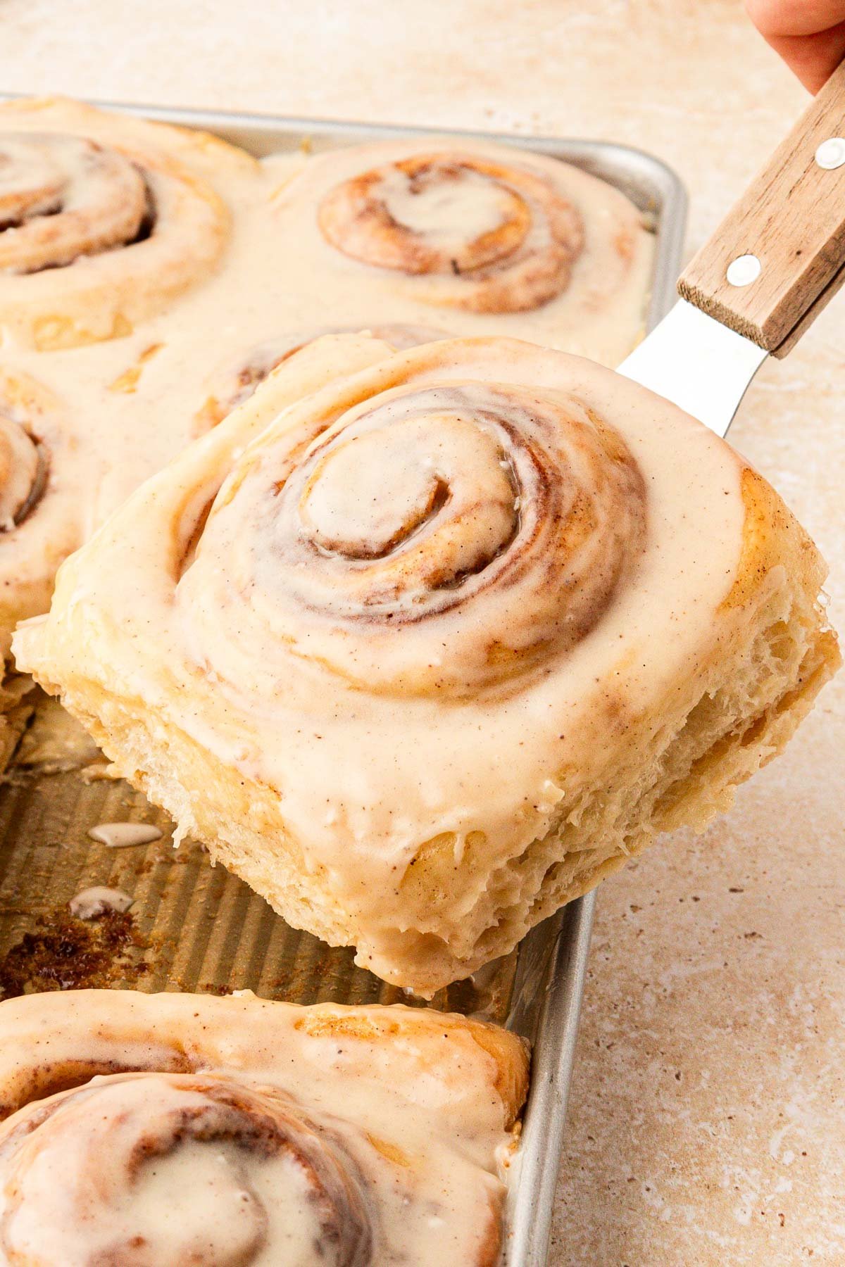 Cinnamon roll being lifted out of a pan with a spatula.