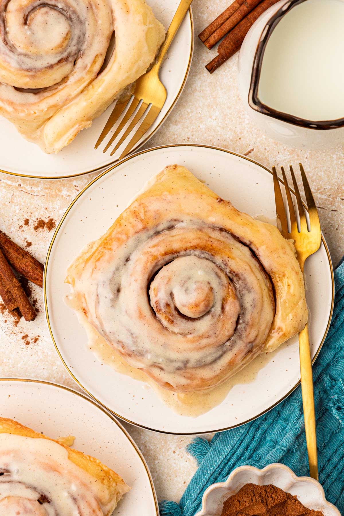 Overhead photo of cinnamon rolls on white plates with gold forks.