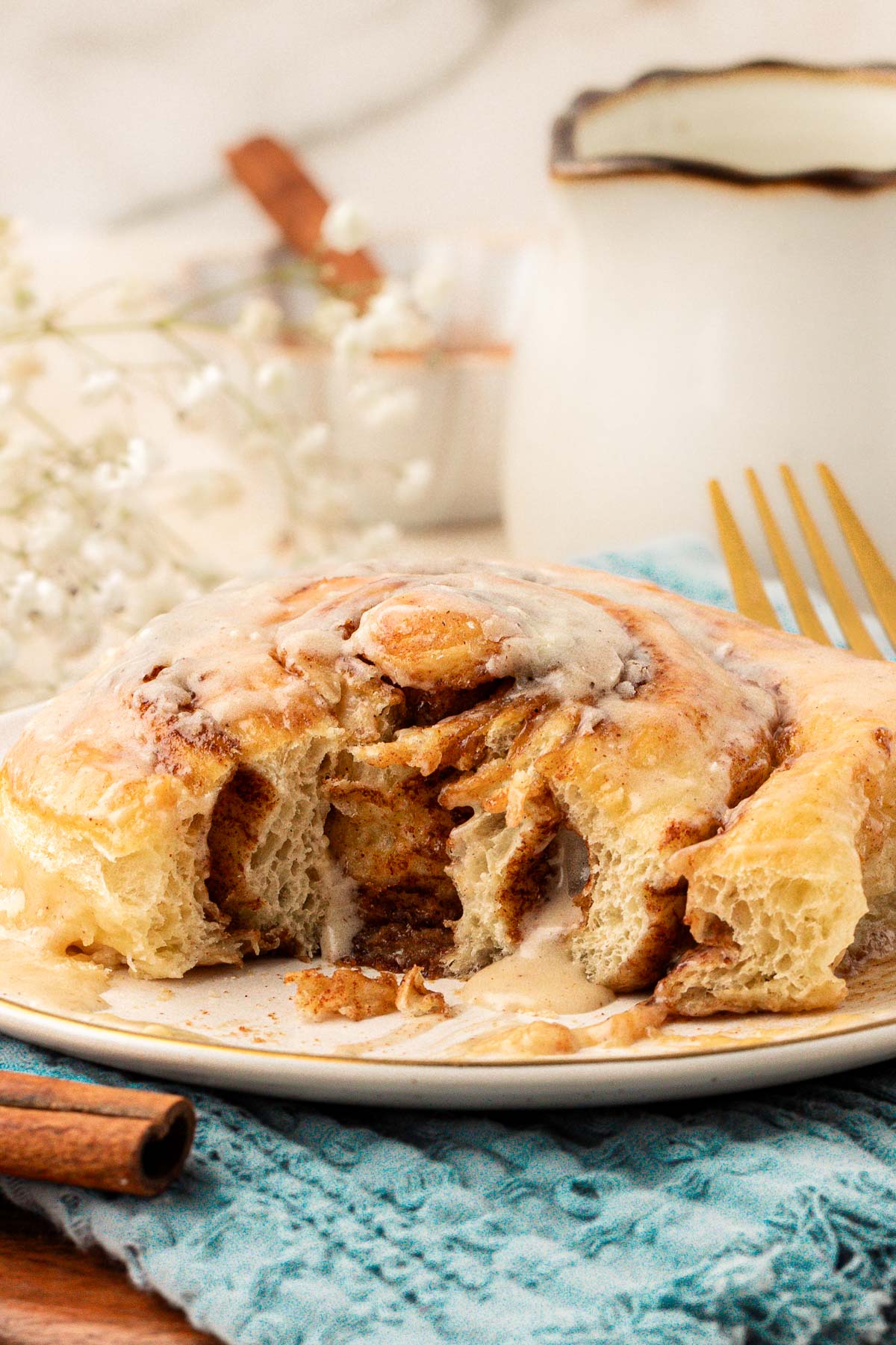 Cinnamon roll on a white plate with a bit missing.