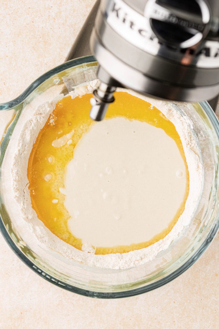 Ingredients being mixed in a glass stand mixer bowl.