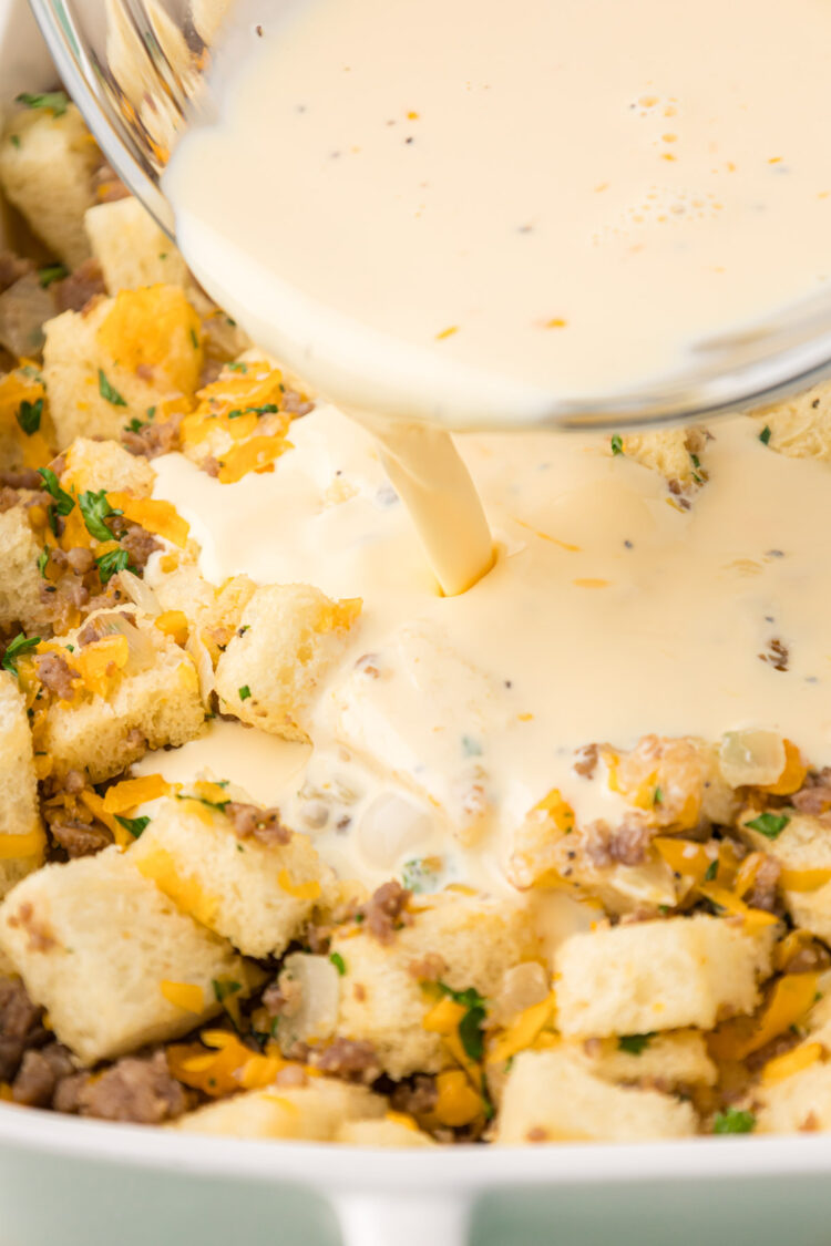 Cream and egg mixture being poured over ingredients in a baking pan to make a sausage strata.