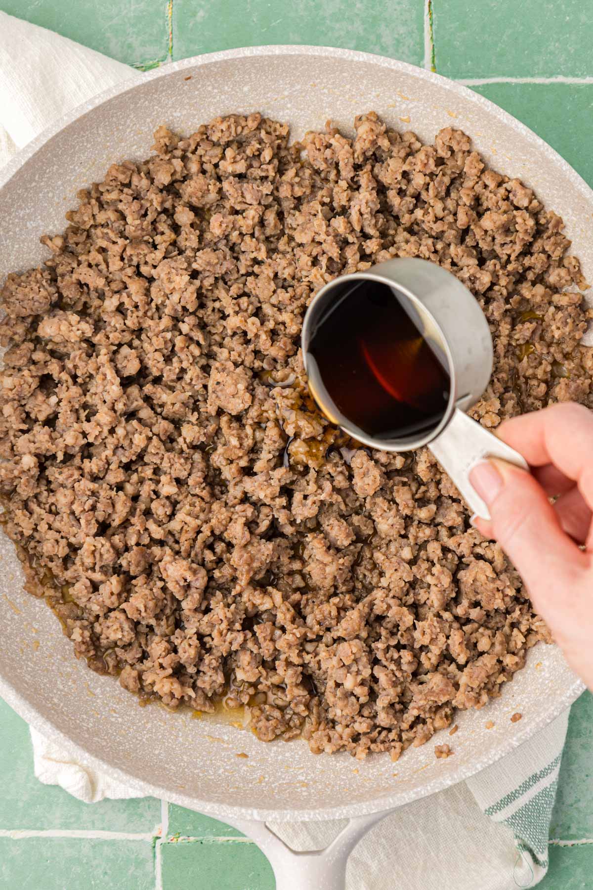 Maple syrup being poured into a skillet with sausage.