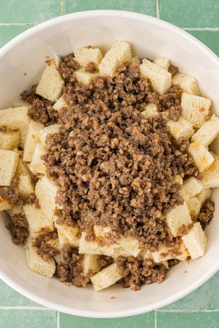 Cooked ground sausage added to a large bowl with cubes of fresh bread.