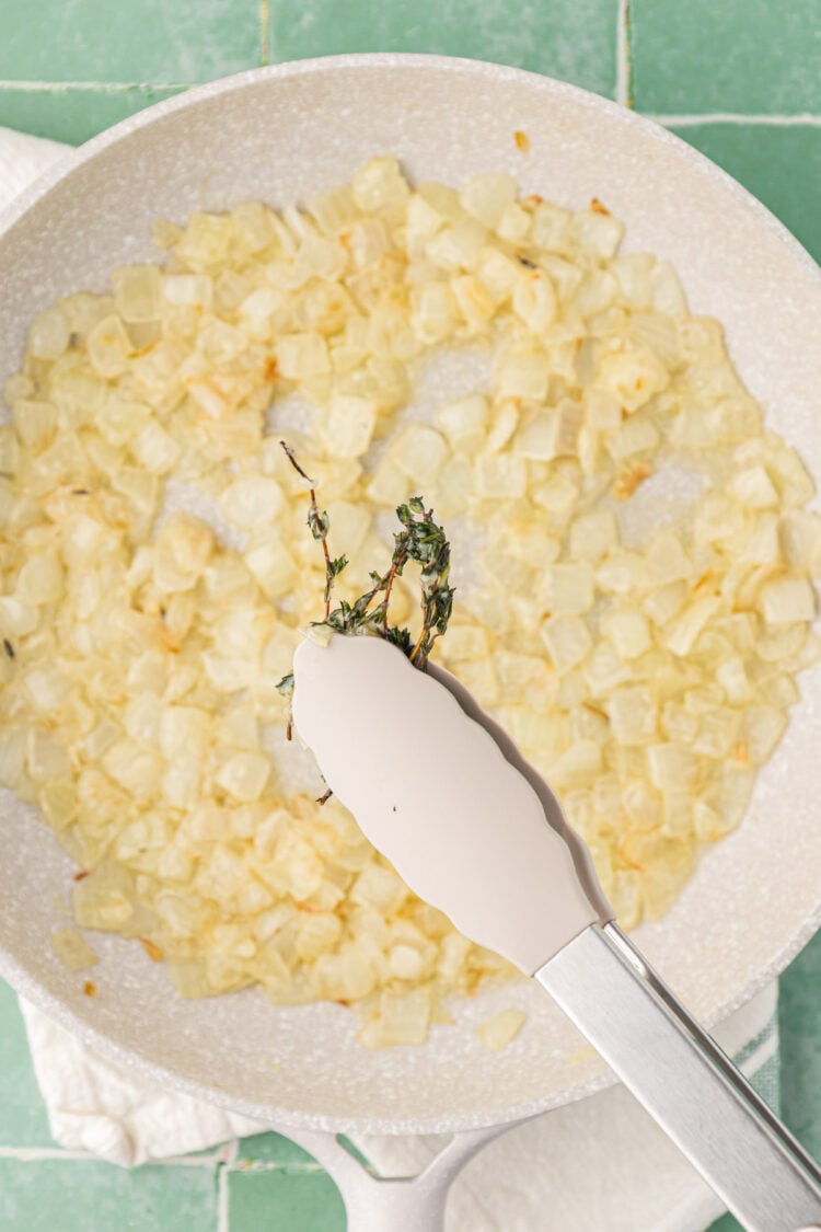 Tongs removing thyme from a skillet.