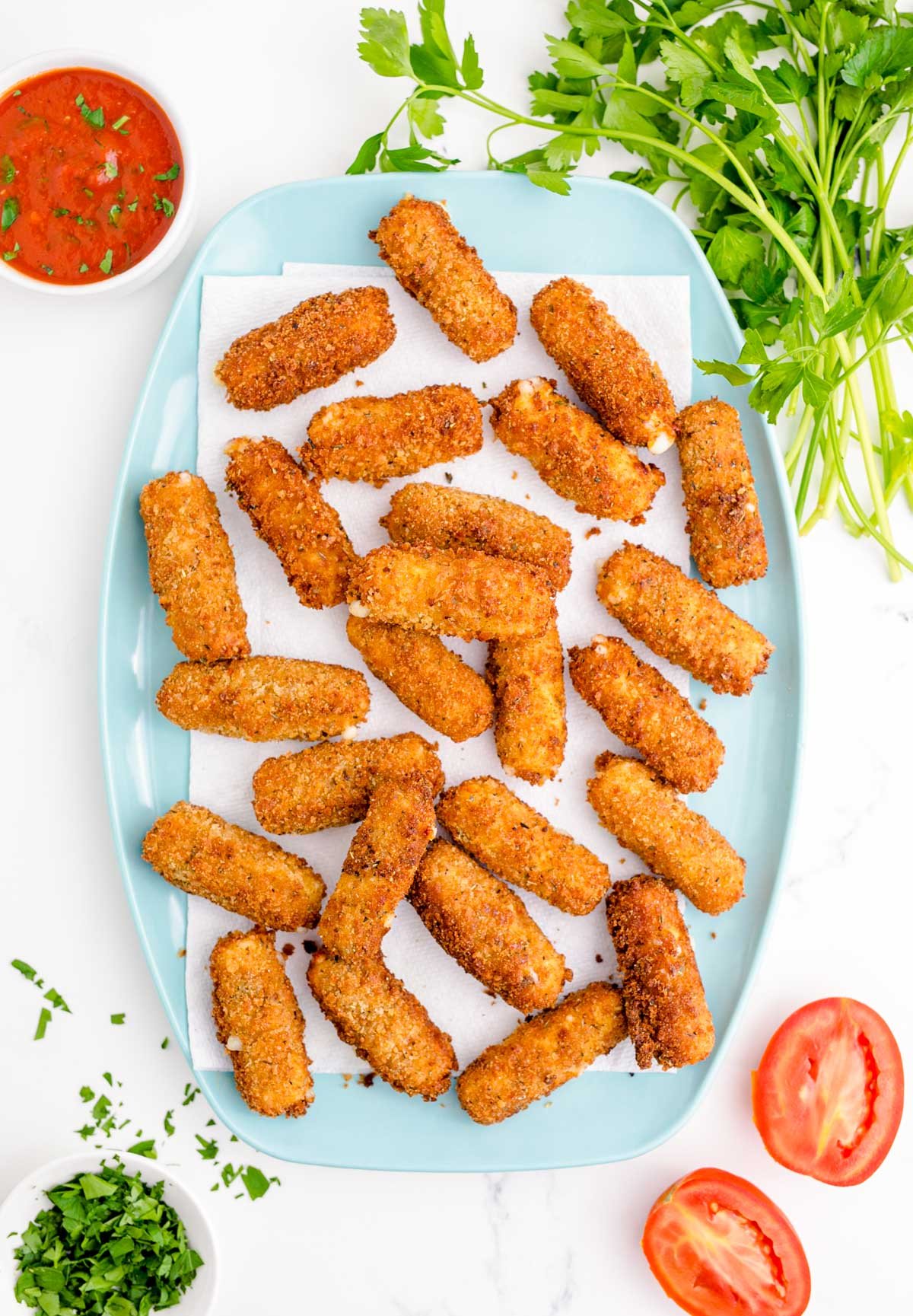 Overhead photo of mozzarella sticks on a paper towel-lined blue plate.