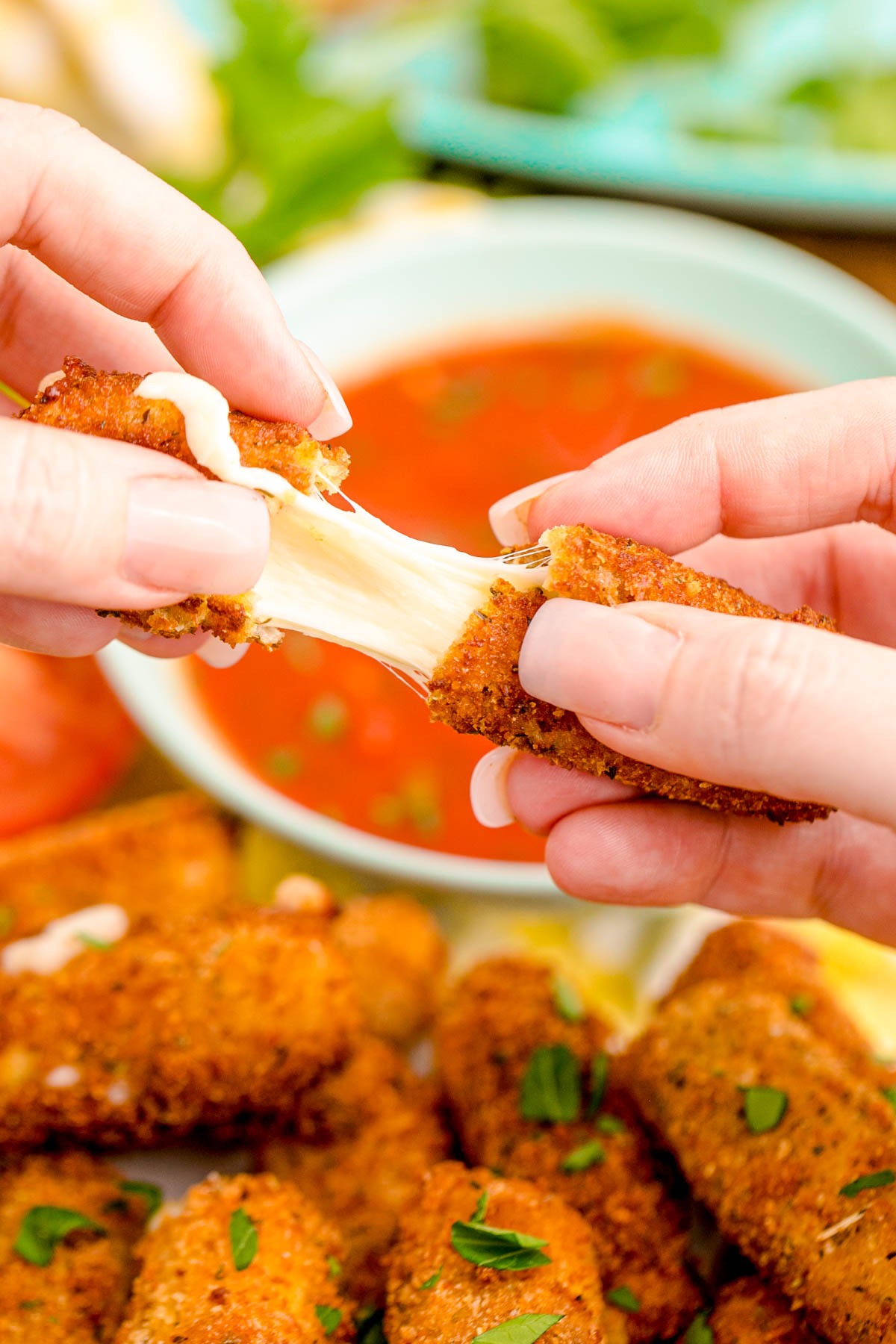 A woman's hand pulling a mozzarella stick apart. 