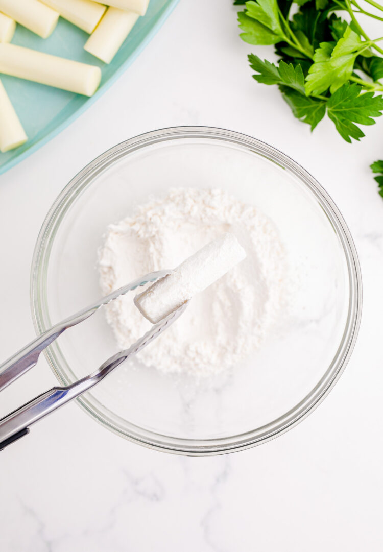 A piece of cheese stick being dipped in flour.