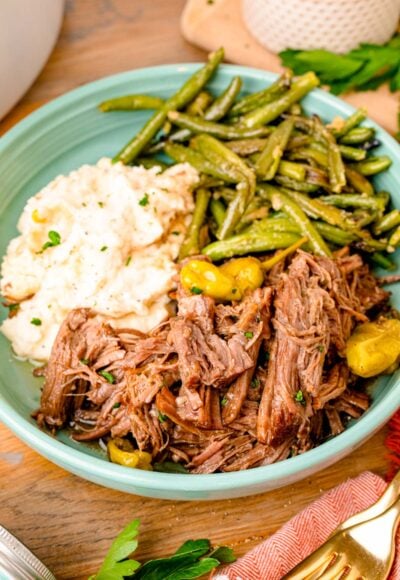 Mississippi pot roast served in a teal bowl with potatoes and green beans.