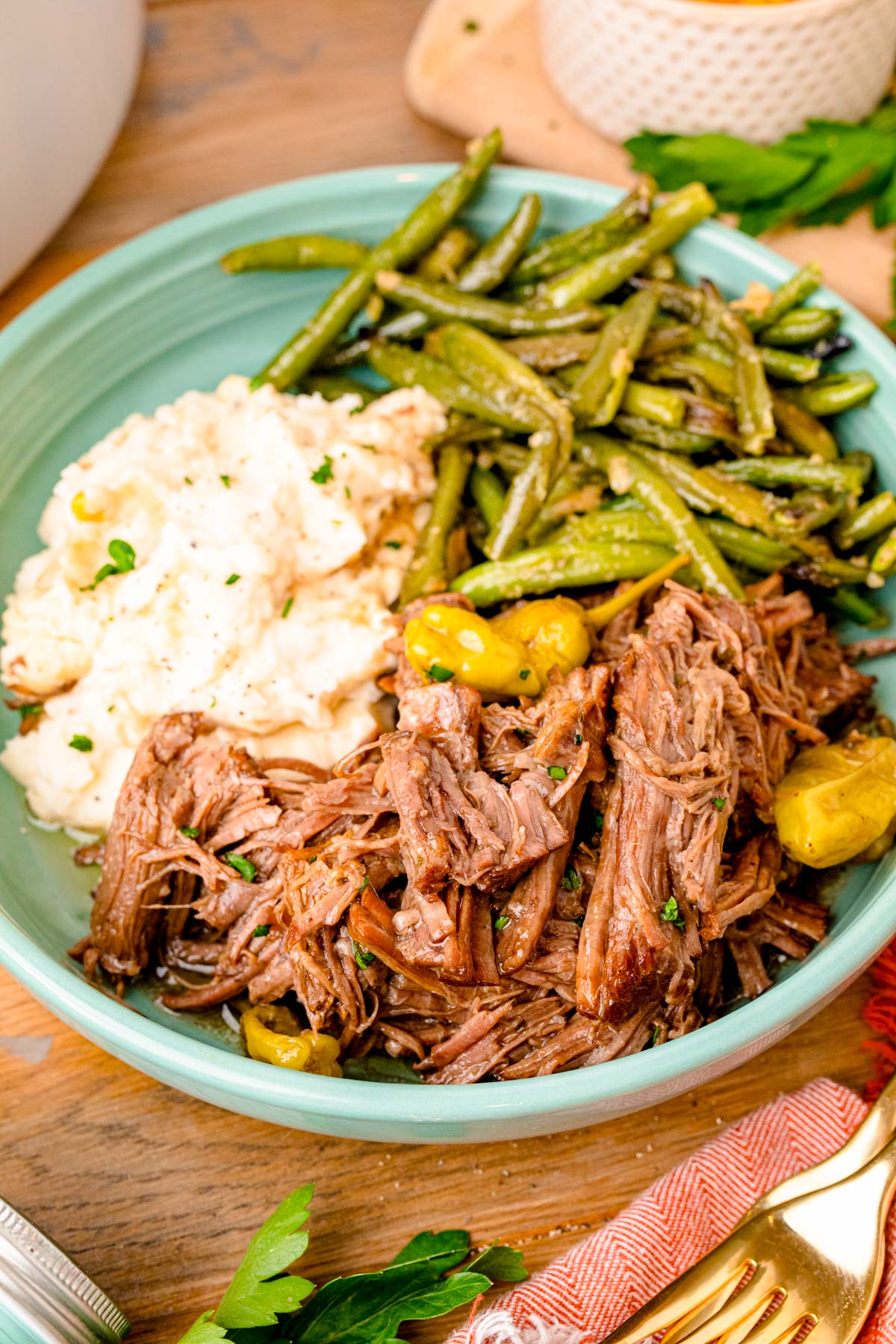 Mississippi pot roast served in a teal bowl with potatoes and green beans.