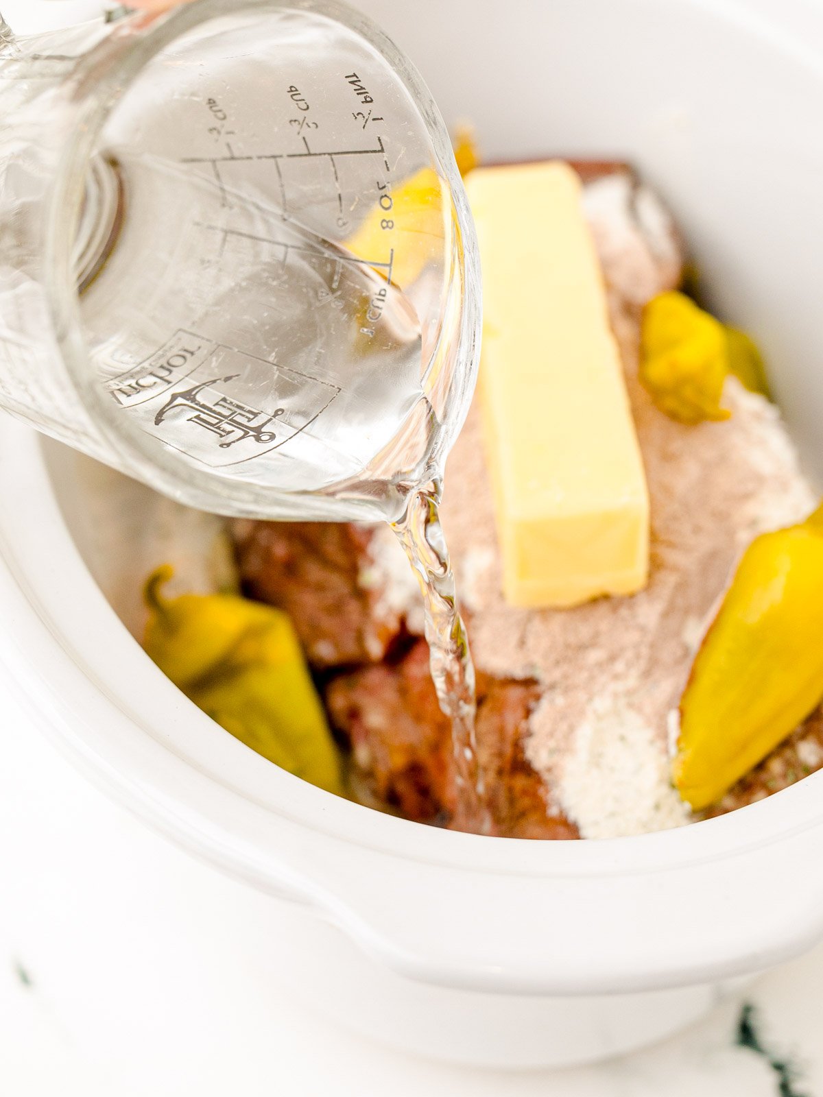 Water is being poured into a slow cooker to make a Mississippi pot roast.